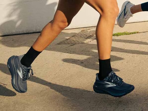 A person in Brooks shoes running on a sunny sidewalk